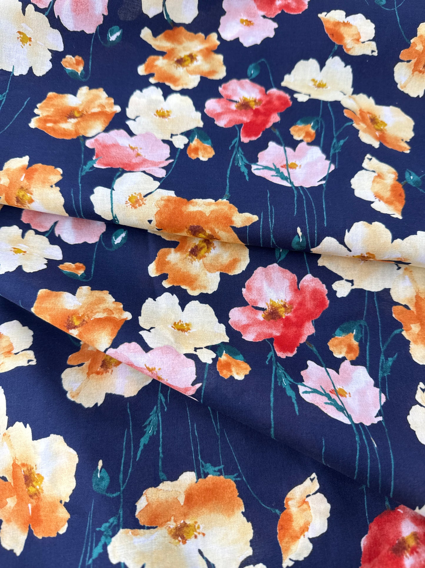 A close-up of a navy blue fabric with a watercolor floral print featuring orange, pink, and cream flowers with green stems.