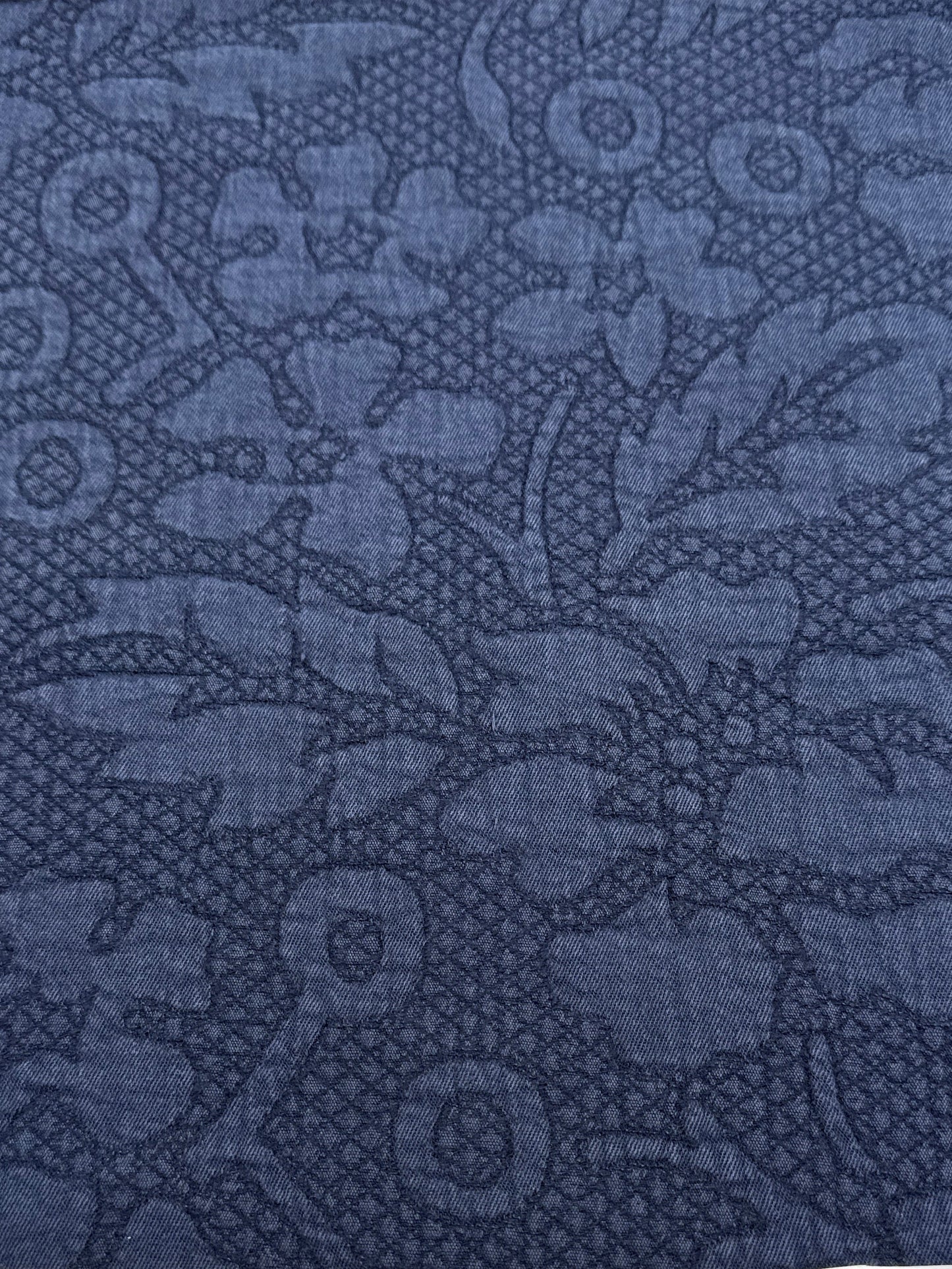 A close-up of a dark blue patterned fabric with a tonal floral and geometric design