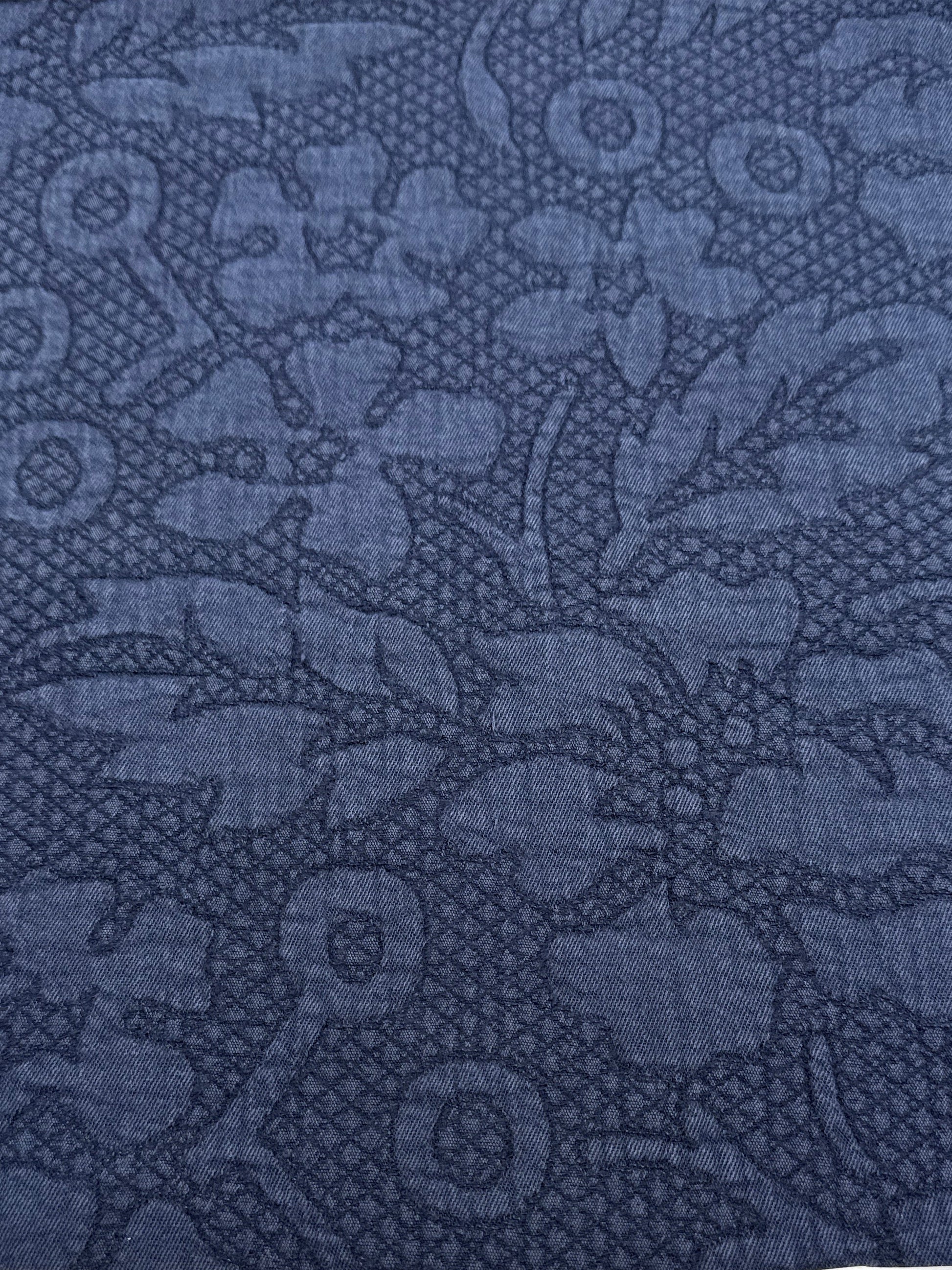 A close-up of a dark blue patterned fabric with a tonal floral and geometric design