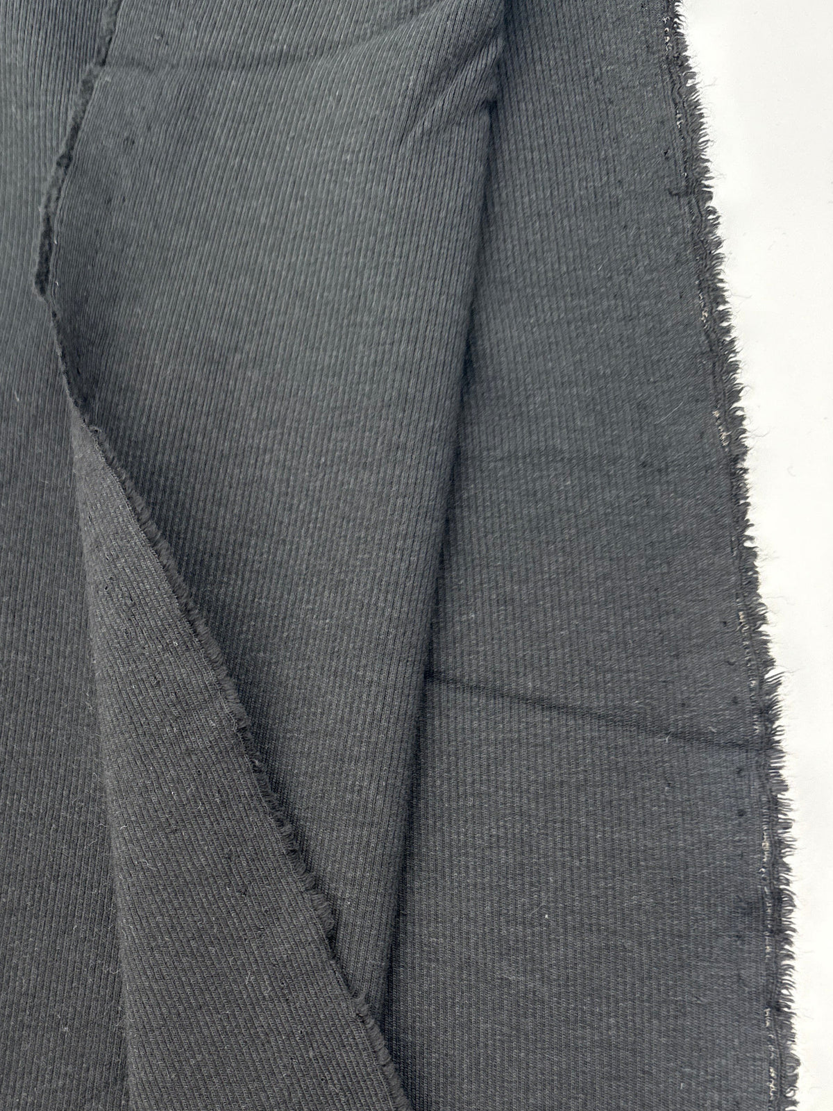 A close-up of black fabric with visible texture and a raw, frayed edge, alongside a white paper label or tag.