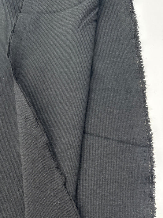 A close-up of black fabric with visible texture and a raw, frayed edge, alongside a white paper label or tag.