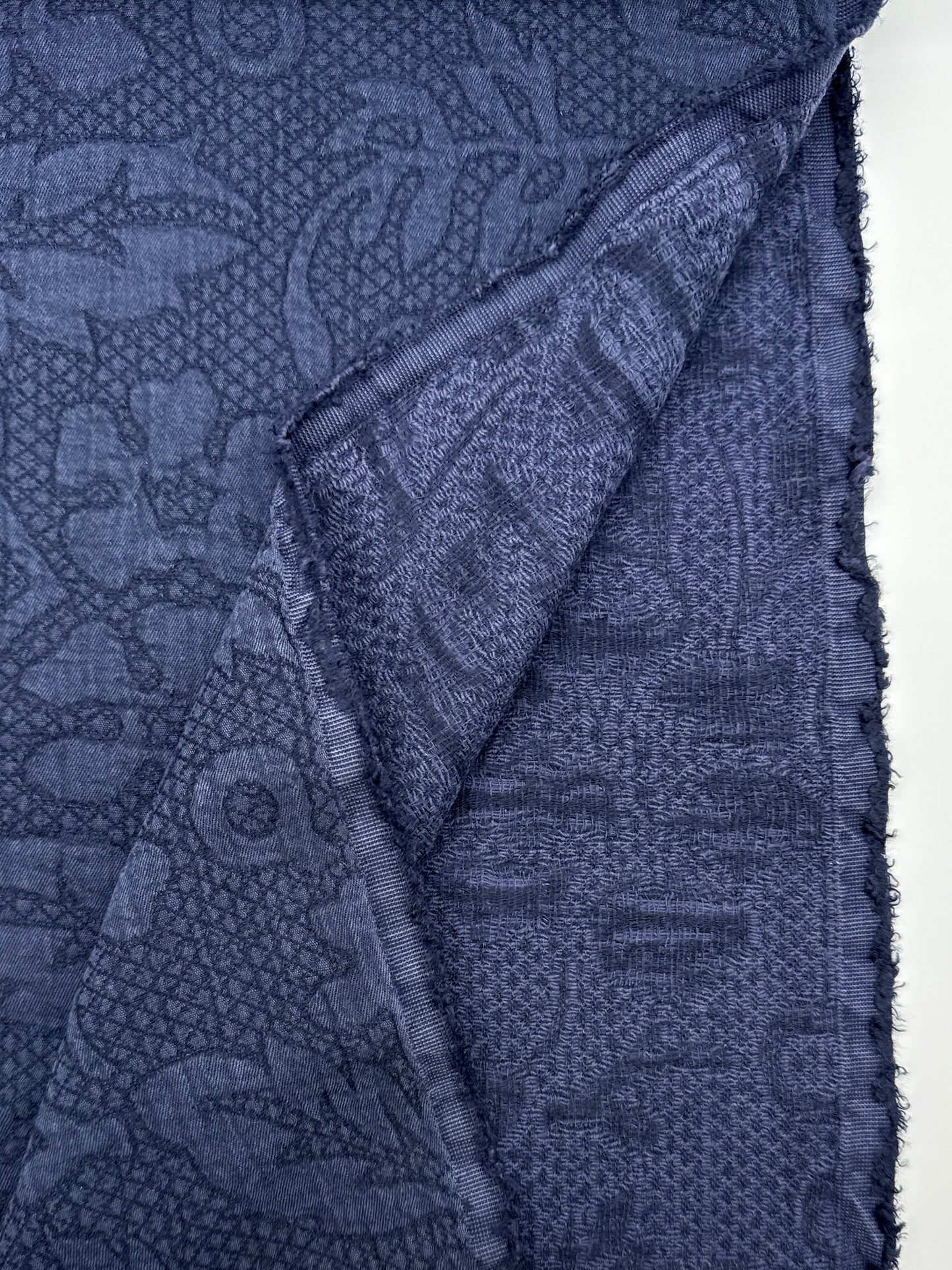 A folded piece of dark blue patterned fabric with a woven paisley and floral design, shown against a white background 