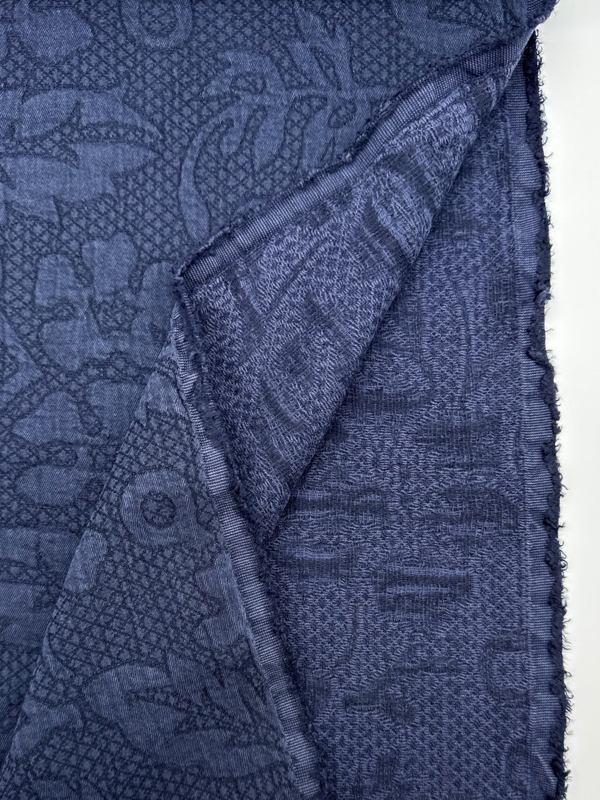 A folded piece of dark blue patterned fabric with a woven paisley and floral design, shown against a white background 