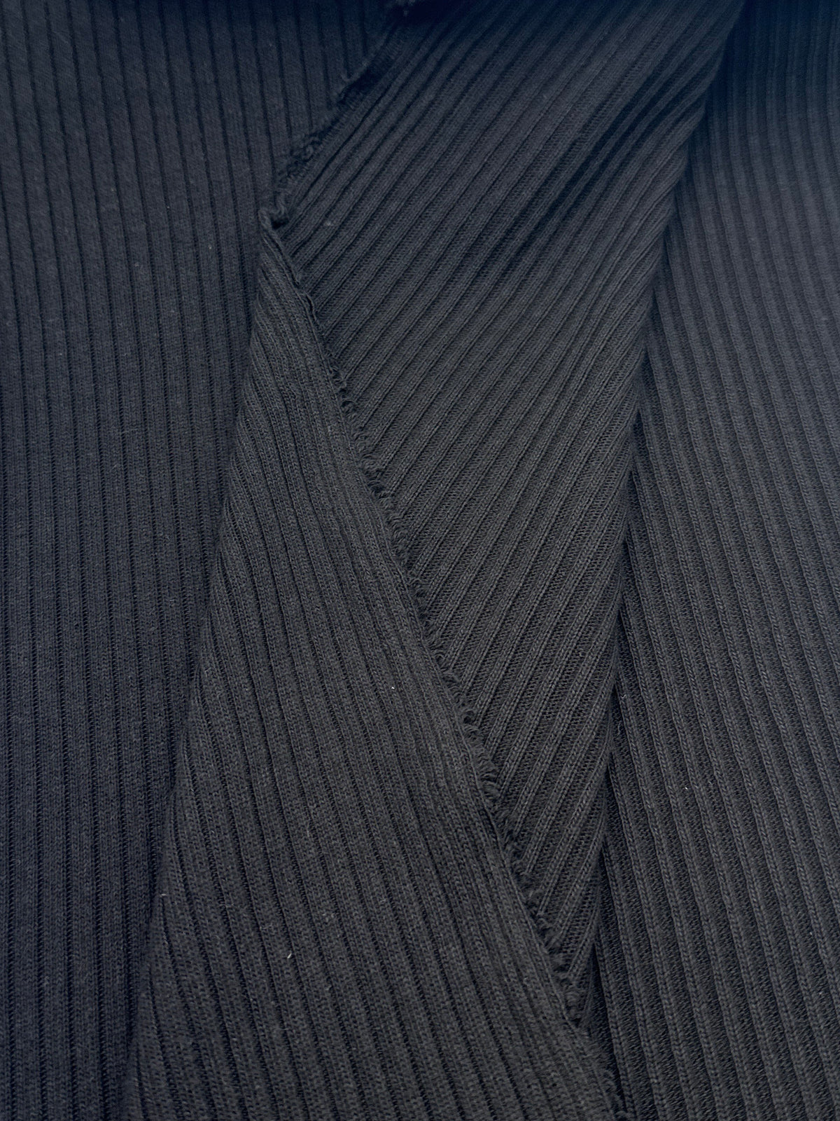 Close-up of a black ribbed knit fabric, likely a sweater or garment, with folded white paper pieces placed on top.